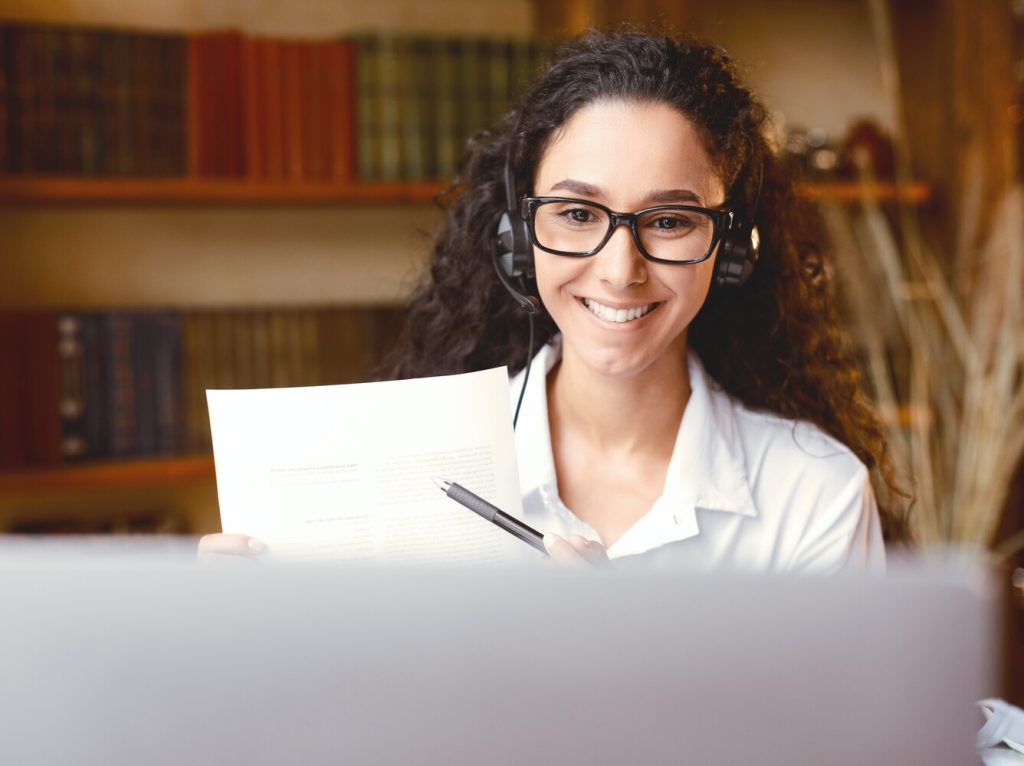 Woman in glasses sitting at desk, having videocall on laptop
