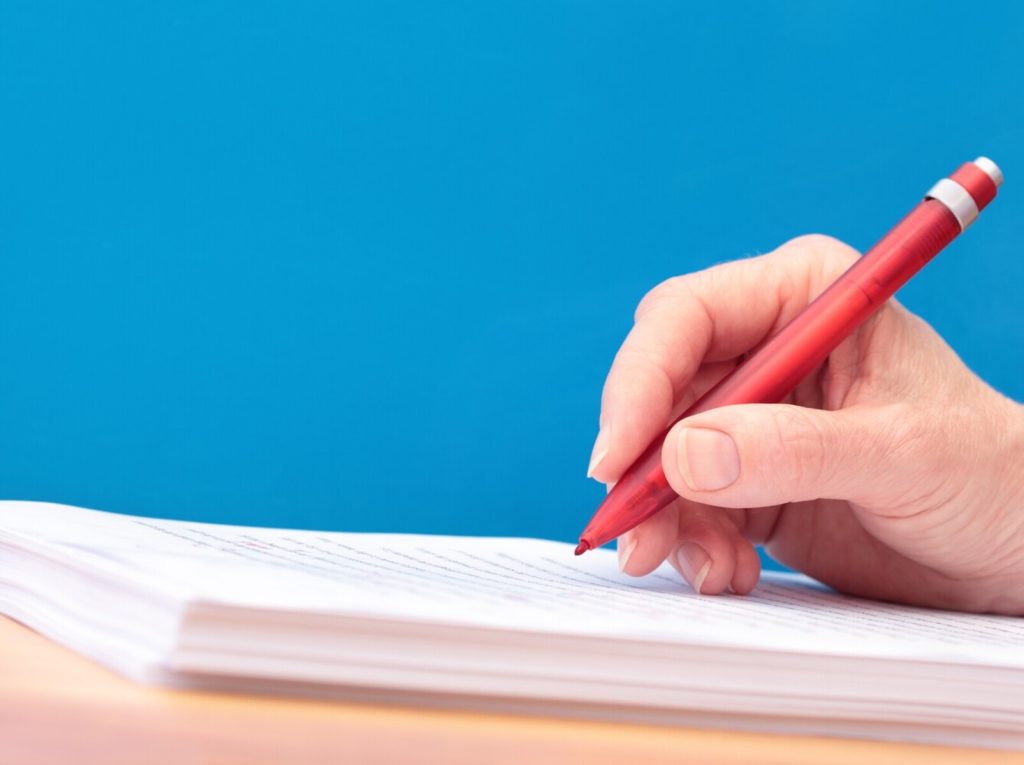 hand holding a red pen and proofreading papers
